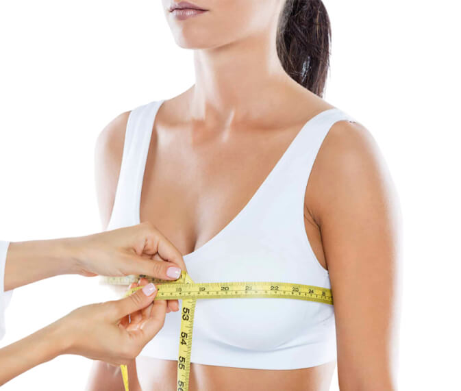 A woman uses a tape measure to accurately determine her bra size, focusing on the measurement process.