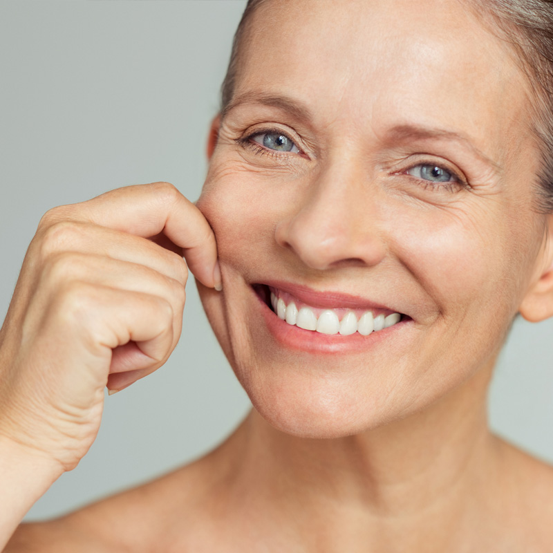 A woman with a joyful expression gently touching her face, radiating happiness and warmth.